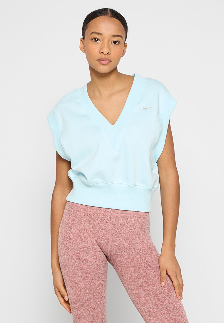 Sweatshirt court bleu clair avec un décolleté en V et des manches courtes. Logo Nike en argent sur la poitrine. Porté avec des leggings texturés roses.