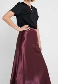 Czarna bluzka z krótkim rękawem i dekoltem z wycięciem typu keyhole, zestawiona z bordową satynową maxi spódnicą o gładkiej, błyszczącej fakturze.