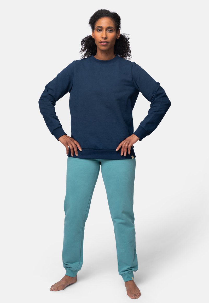 Navyblauwe katoenen sweatshirt met lange mouwen, ronde hals en geribbelde manchetten, gecombineerd met lichtgroene sweatpants met een taps toelopende pasvorm en een gladde textuur.