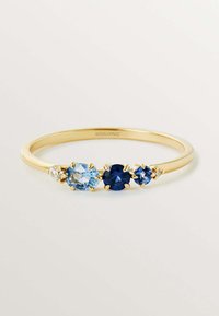 Anillo de oro amarillo con tres piedras: una redonda azul claro, una redonda azul oscuro y un diamante redondo transparente, todas engastadas en garras.