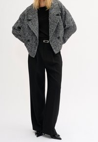 Svart och vit houndstooth oversized jacka med strukturerade axlar, tillsammans med högmidjade svarta byxor och spetsiga svarta skor.