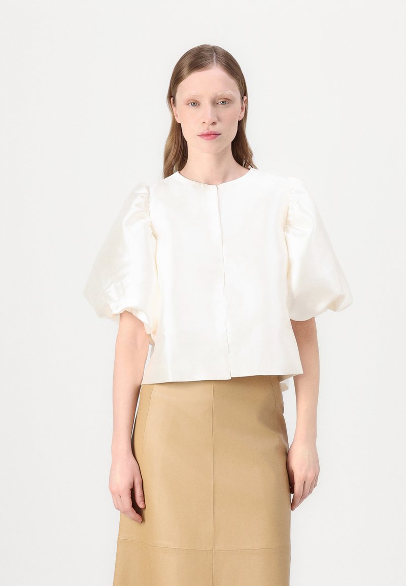 White satin top with puff sleeves, round neckline, and front button closure, paired with a beige skirt, smooth texture throughout.