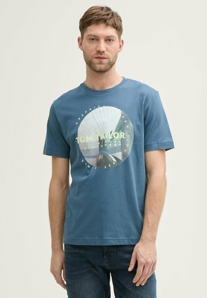 Camiseta azul de algodón con un estampado gráfico redondo que presenta el texto "TOM TAILOR" y un diseño fotográfico, de manga corta y cuello redondo.