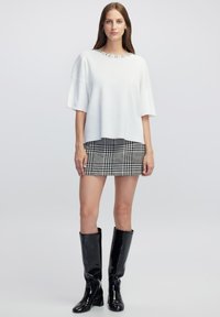 Blusa blanca de corte holgado con un escote adornado con cuentas, combinada con una falda mini de pata de gallo en blanco y negro y botas de látex a la rodilla.