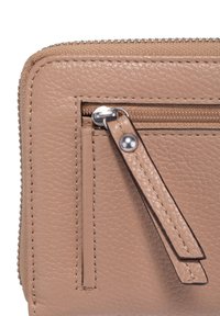 Pogled od blizu na kut rub beige kožne novčanike, koji prikazuje metalni zip s kožnom ručkom i vidljivim detaljima �šivanja.