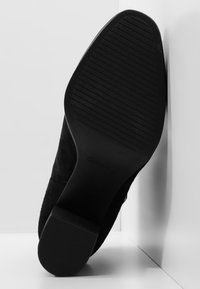 Stivaletto in suede nero con suola in gomma, dotato di fondo texturizzato per una migliore aderenza. Il tacco è basso e il design è snello.