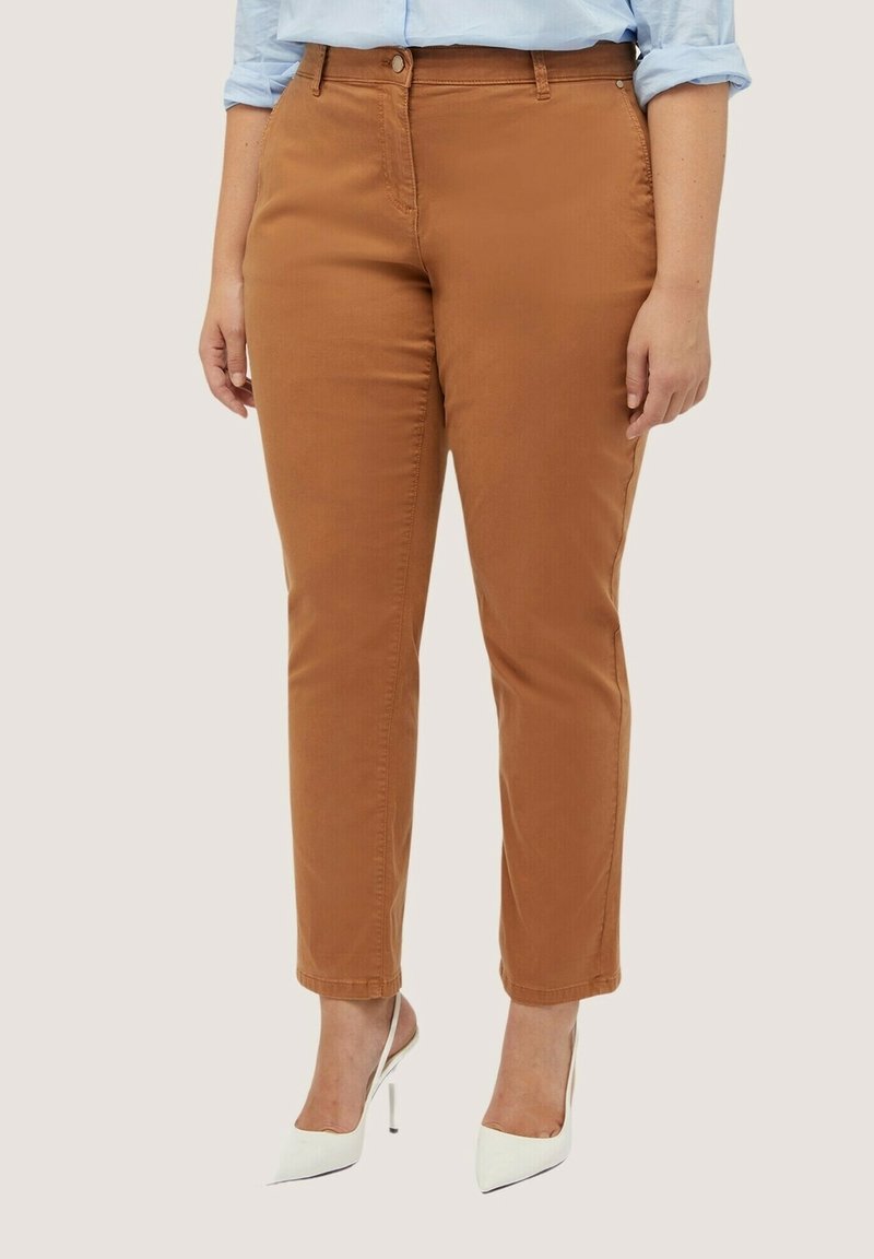 Pantalon en coton marron avec une coupe slim, doté de poches avant et d'une fermeture à bouton. Associé à des escarpins blancs.