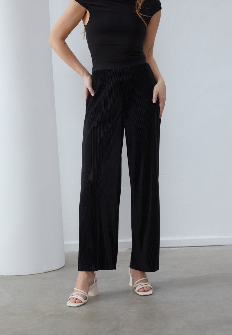 Pantaloni a gamba larga neri a costine con vita alta e cintura liscia. Indossati con una maglietta nera aderente e sandali con tacco leggeri.
