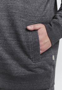 Mörkgrå huvtröja med strukturerad tyg. Har en framficka, ribbade ärmmuddar och en liten "BLEND"-etikett på sidan.