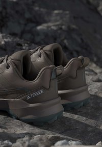Para brązowych butów do trekkingu Adidas Terrex odpoczywająca na skalistym podłożu z teksturowanymi podeszwami i materiałowymi pętelkami na piętach.