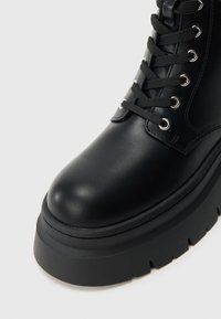 Czarny botek za kostkę wykonany z gładkiej skóry, z okrągłym noskiem, grubą podeszwą na platformie oraz sznurowaniem z srebrnymi oczkami.