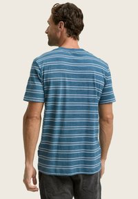 Camiseta de algodón a rayas azul y blanca con mangas cortas, cuello redondo y un corte relajado, mostrando la espalda y los hombros de un modelo.