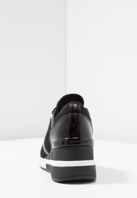 Baskets noires à finition texturée, dotées d'une tige en mesh, d'accents brillants et d'une semelle blanche épaisse. Marquage visible sur le talon.