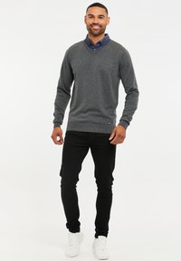 Maglione grigio a V con una texture liscia, indossato sopra una camicia blu con colletto. Abbinato a pantaloni neri e sneakers bianche. Design semplice.