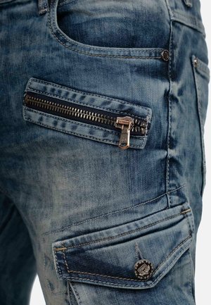 Denim-Jeans in blassem Blau mit strukturierter Oberfläche, ausgestattet mit einer Reißverschlusstasche und Metallakzenten. Taillierte Passform mit verstärkten Nähten.