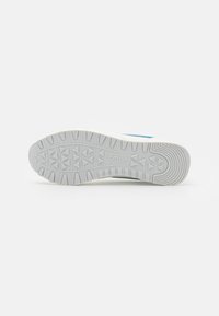 Vit sportskor med en texturerad grå gummisula och blå detaljer, som visar en stödjande och hållbar design som är lämplig för olika aktiviteter.