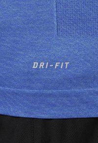 Niebieski materiał Dri-FIT o teksturowanej powierzchni; produkt ma kontrastującą czarną lamówkę i logo Dri-FIT w białym kolorze na dole.