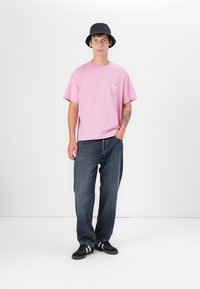 Lyserød bomulds t-shirt med korte ærmer, mørke denimjeans, sort bucket hat og sorte sneakers med hvide striber. Simpelt design, afslappet pasform.