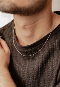 Deux colliers en argent superposés, avec des chaînes fines présentant des détails subtils, reposant sur un pull noir texturé.