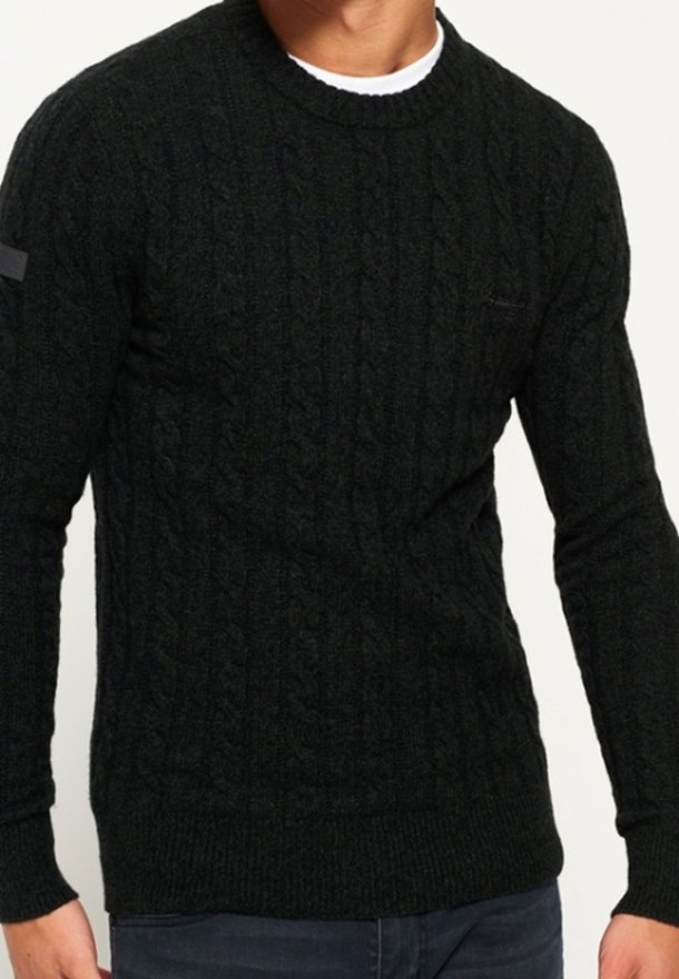 Maglione a maglia cable verde scuro con scollatura rotonda e polsini a costine. Presenta una piccola toppa sul petto. Texture morbida e design aderente.