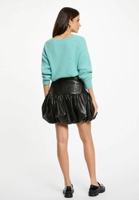 Un maglione lavorato a maglia di colore azzurro chiaro abbinato a una gonna a bolle in pelle nera con un design plissettato, indossato con scarpe nere.
