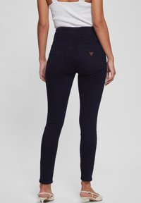 Vysokým pasem, tmavě modré skinny džíny s hladkým povrchem, dvěma zadními kapsami a trojúhelníkovým koženým detailem.