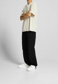 Beżowy, luźny t-shirt oversize, czarne spodnie cargo z kieszeniami oraz białe sneakersy. Prosty design, bawełniany materiał, luźny krój.