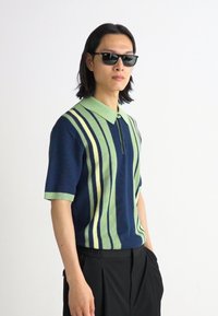Polo cu mânecă scurtă, cu dungi verticale bleumarin, verde și galben, cu un guler cu butoane și un material tricotat texturat.