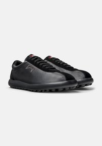 Black sneakers made of leather with a smooth finish and textured panels. Rounded toe, black rubber sole with circular grip points, and laces.