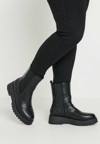 Zwarte leren enkelboots met elastische zijpanelen en een ritsluiting. Chunky rubberen zool met gestructureerde grip. Laag hakontwerp.