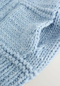 Tissu tricoté bleu clair avec un motif texturé, présentant des mailles épaisses et proéminentes ainsi qu'une finition douce et duveteuse.