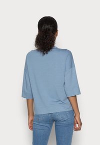 Top azzurro chiaro a maniche corte con scollatura rotonda e vestibilità rilassata. Realizzato in tessuto morbido e liscio. Abbinato a jeans in denim chiaro.