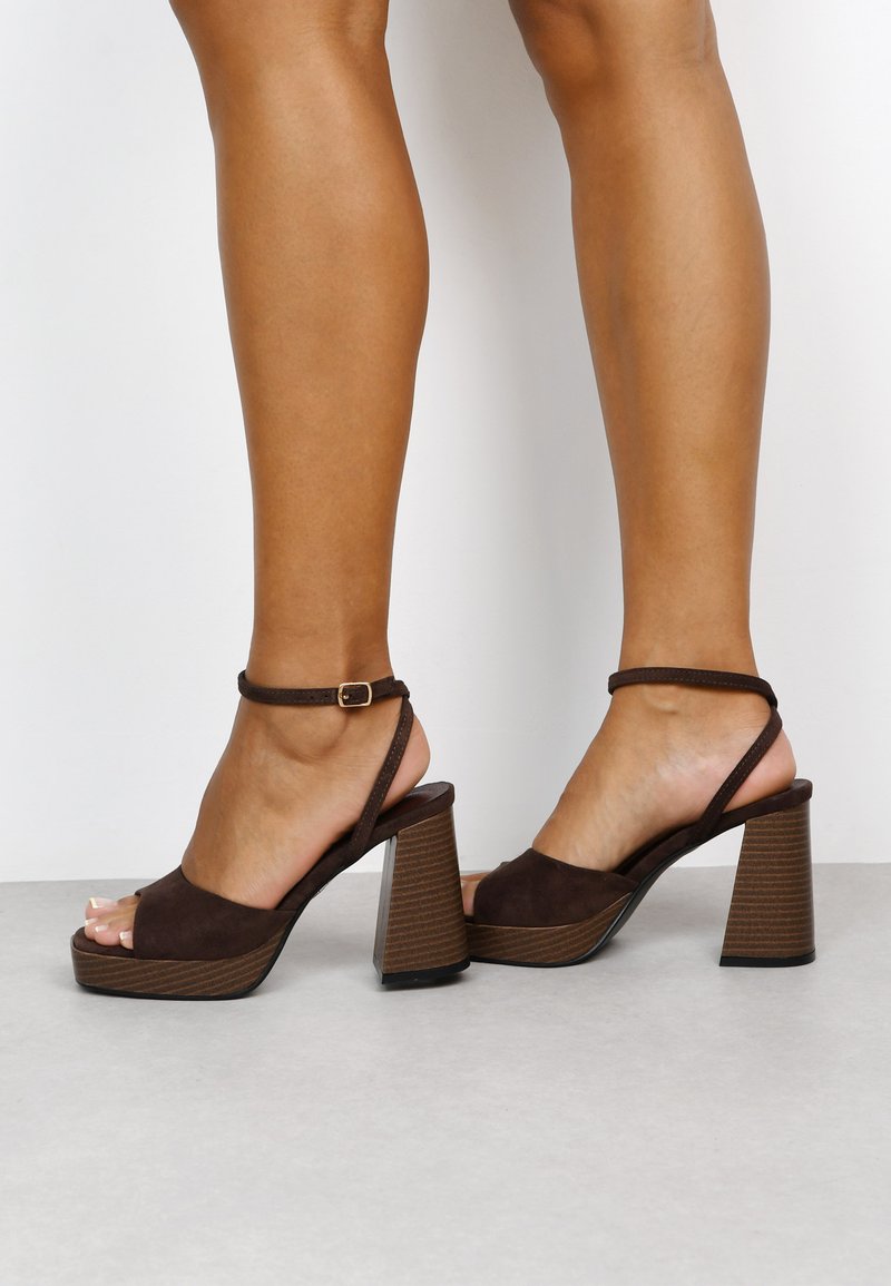 Brown suede sandals with a peep toe, ankle strap, and a textured brown block heel. Features a smooth upper with a minimalist design.
