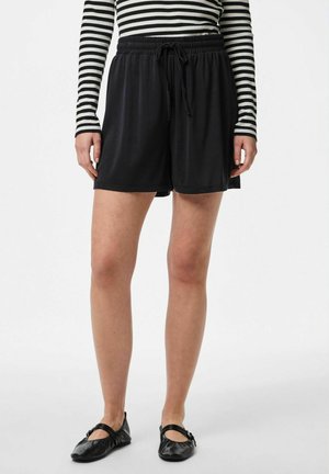 Pantaloni shorts neri in tessuto con vita elastica e cordoncino regolabile. Texture liscia, lunghezza fino al ginocchio. Abbinati a scarpe nere senza tacco.