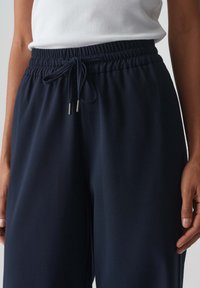 Pantalons de survêtement bleu marine en tissu doux, dotés d'une taille élastique avec cordon de serrage et embouts métalliques, offrant une coupe décontractée.