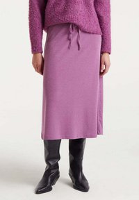 Falda morada de longitud media en tejido suave con cintura ajustable, combinada con elegantes botas negras hasta la rodilla. Top de punto texturizado en color rosa.