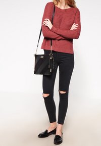 Bordowy dzianinowy sweter, czarne przetarte spodnie skinny, błyszczące czarne loafersy oraz czarna torba o skośnym wzorze z złotym akcentem.