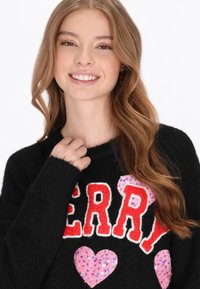 Pulover negru cu litere roșii "MERRY", accentuat de inimioare roz cu paiete. Textură moale, guler rotund și mâneci lungi.