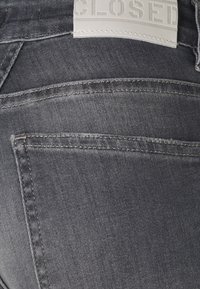 Ciemnoszare dżinsy z delikatną teksturą, z skórzaną metką na pasie z napisem "CLOSED" wklęsłym. Brak widocznych elementów metalowych.