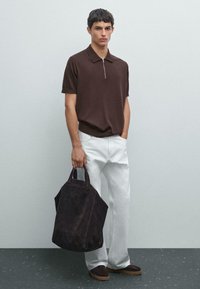 Polo shirt marrone con colletto a zip, pantaloni bianchi larghi e una borsa a tracolla in suede scuro, caratterizzata da una texture morbida e una forma angolare.