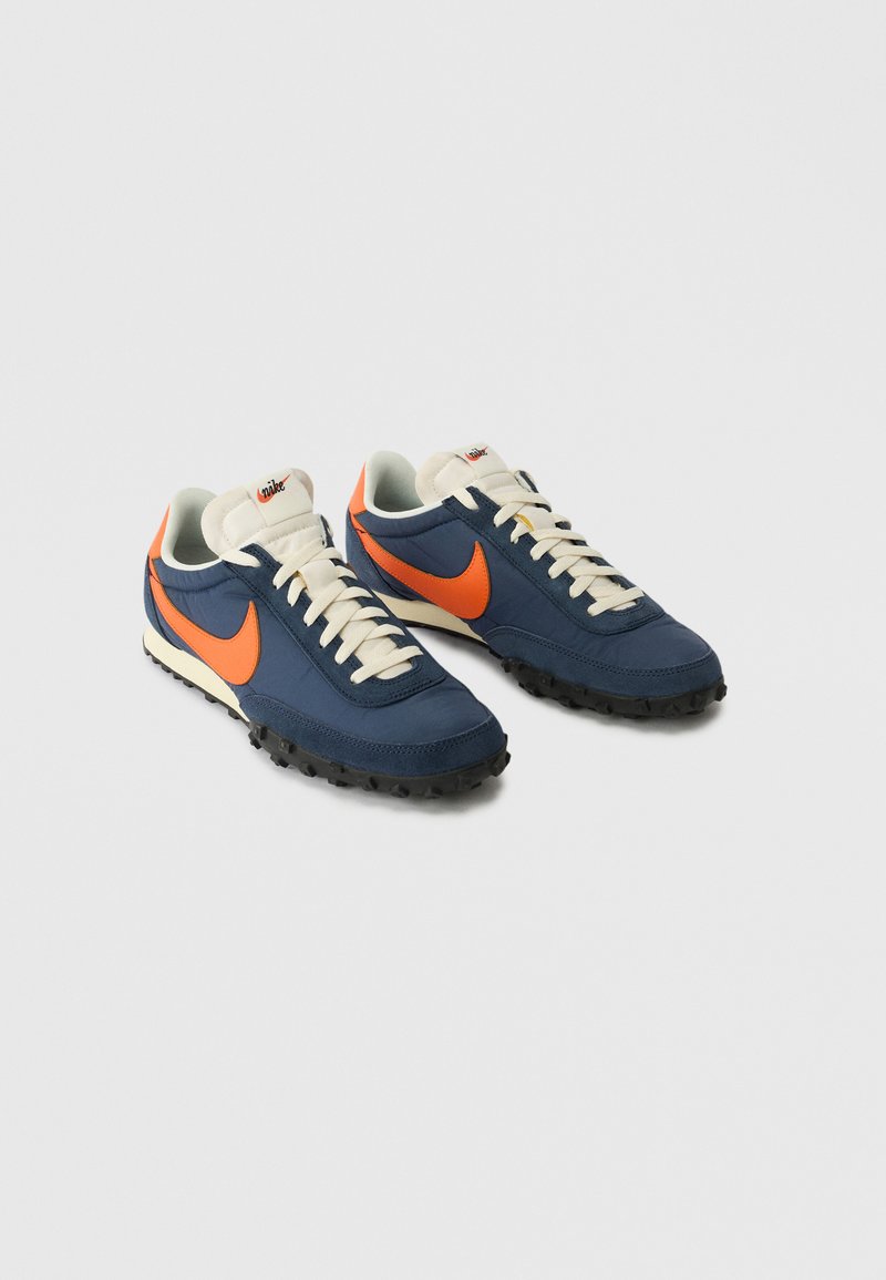 Blaue und orange Sport Schuhe mit einem strukturierten marineblauen Obermaterial, cremefarbenen Schnürsenkeln und einer schwarzen Gummisohle; mit einem auffälligen Nike-Swoosh.