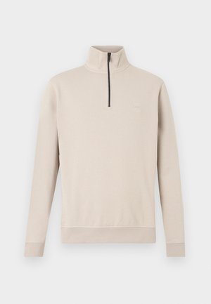 Beige-collegepaita, jossa on korkea kaulus, puolivetoketju edessä ja resorit hihansuissa. Pehmeä kangas, jossa hienovarainen tekstuuri ja pieni logo rinnassa.