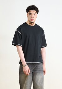 T-shirt noir à manches courtes avec des détails en fil argenté et une coupe décontractée, associé à un jean large gris. Design simple et tissu respirant.