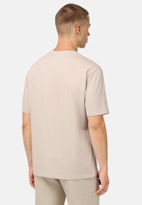 Šviesiai ruda t-shirt su apvaliu kaklu ir trumpomis rankovėmis, pagaminta iš lygaus audinio; paprastas dizainas be matomų raštų ar detalių.