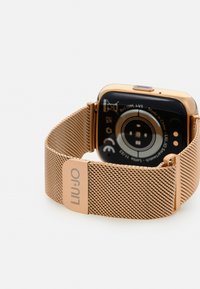 Smartwatch color oro rosato con cinturino in metallo a rete con chiusura. Il display arrotondato ha un fondo nero con marcature minime sul retro.