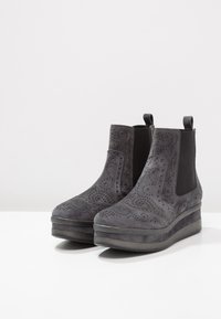 Botines de ante negros con detalles perforados, paneles laterales elásticos y una suela de plataforma gruesa para mayor altura.