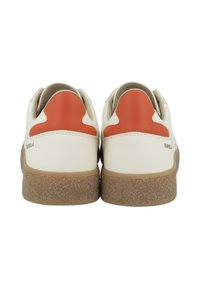 White leather sneakers with orange heel accents, textured tan rubber sole, and simple design. Branding visible near the heel area.