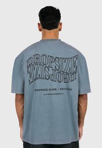 Gray oversized t-shirt features a bold, distorted black text design "DROPSIZE" on the back, with "DROPSIZE CLUB / EST.2020" below.