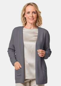 Grijze cardigan met een open voorkant, lange mouwen en twee voorzakken. Zachte textuur en een relaxte pasvorm over een lichte, zijdeachtige top.