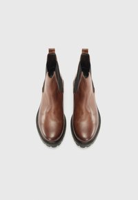 Bottines en cuir marron avec des panneaux élastiques sur les côtés et des boucles. Présentent un bout arrondi et une semelle en caoutchouc noir contrastante.